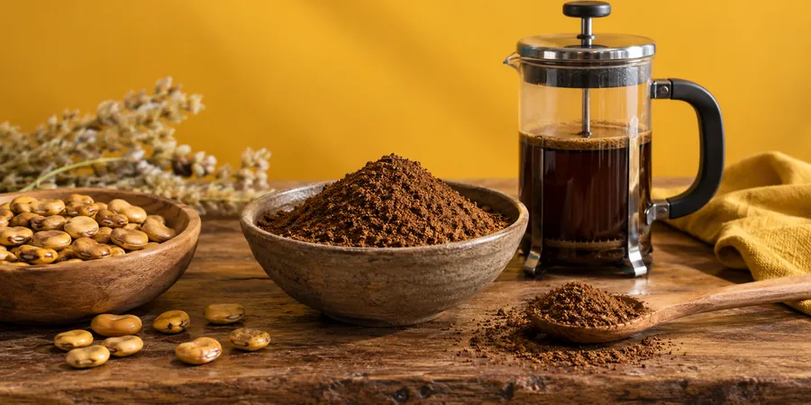 Geröstete Lupinensamen, gemahlenes Pulver und eine French Press auf einem Holztisch